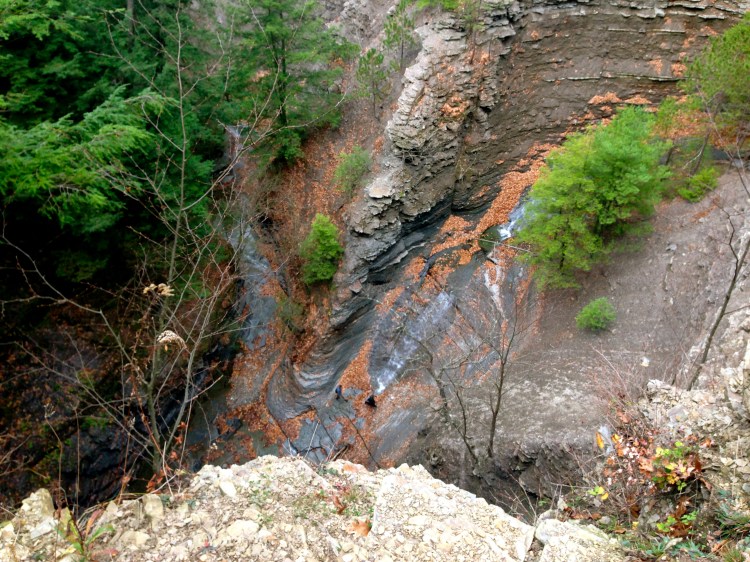 Two men hiking through the gully below, approaching a steep waterfall.